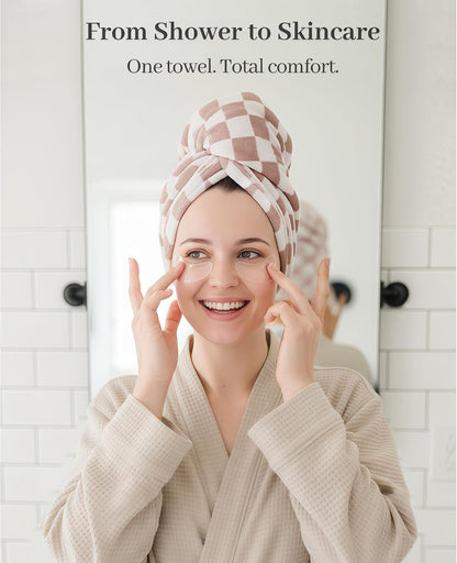Smiling woman in a waffle-knit robe applying skincare, wearing a pink and white checkered hair towel wrap twisted on her head. Text reads 'From Shower to Skincare - One towel. Total comfort.'