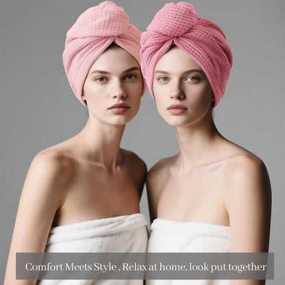 Two women each wearing a pink waffle-weave hair towel turban, wrapped and knotted on top of the head. Both wear white towels and face forward against a gray background. Text reads: Comfort Meets Style, Relax at home, look put together.