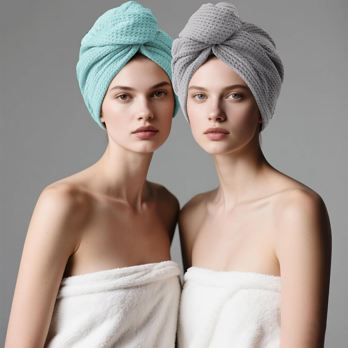 Two models each wearing a twisted hair towel turban wrap, one in light teal/cyan and one in gray, both with visible waffle-weave texture. Models wear white towels and face forward against a neutral gray background.