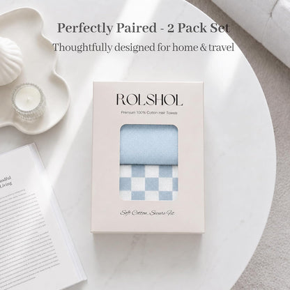 ROLSHOL branded gift box containing 2 cotton hair towels in light blue: one solid and one blue-and-white checkerboard pattern. Box reads 'Premium 100% Cotton Hair Towels' and 'Soft Cotton, Secure Fit.' Overlay text: 'Perfectly Paired - 2 Pack Set.'