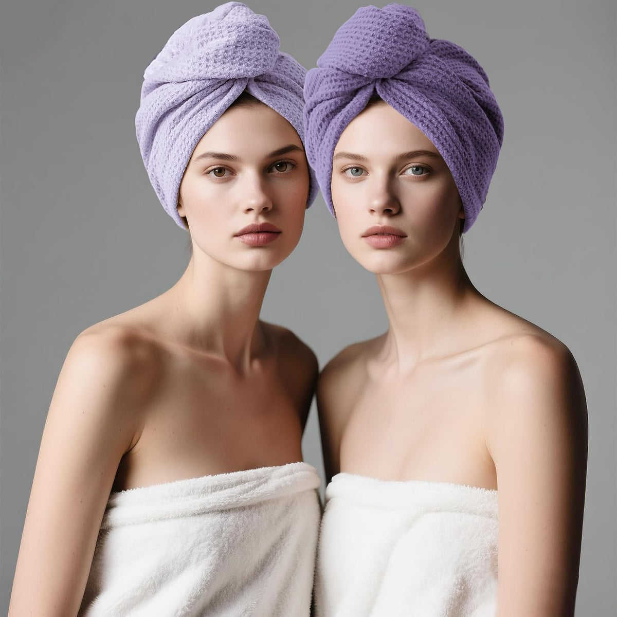 Two models each wearing a hair towel turban wrapped on their heads, one in light lavender and one in deeper purple, both with waffle-weave texture. Models wear white towels and face forward against a gray background.