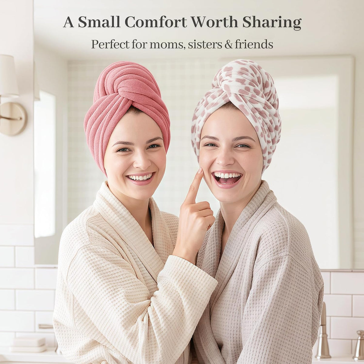 Two smiling women in waffle-knit robes wearing hair towel wraps in a bathroom setting. One wears a solid pink wrap, the other a white wrap with pink leopard print. Text reads 'A Small Comfort Worth Sharing - Perfect for moms, sisters & friends'.