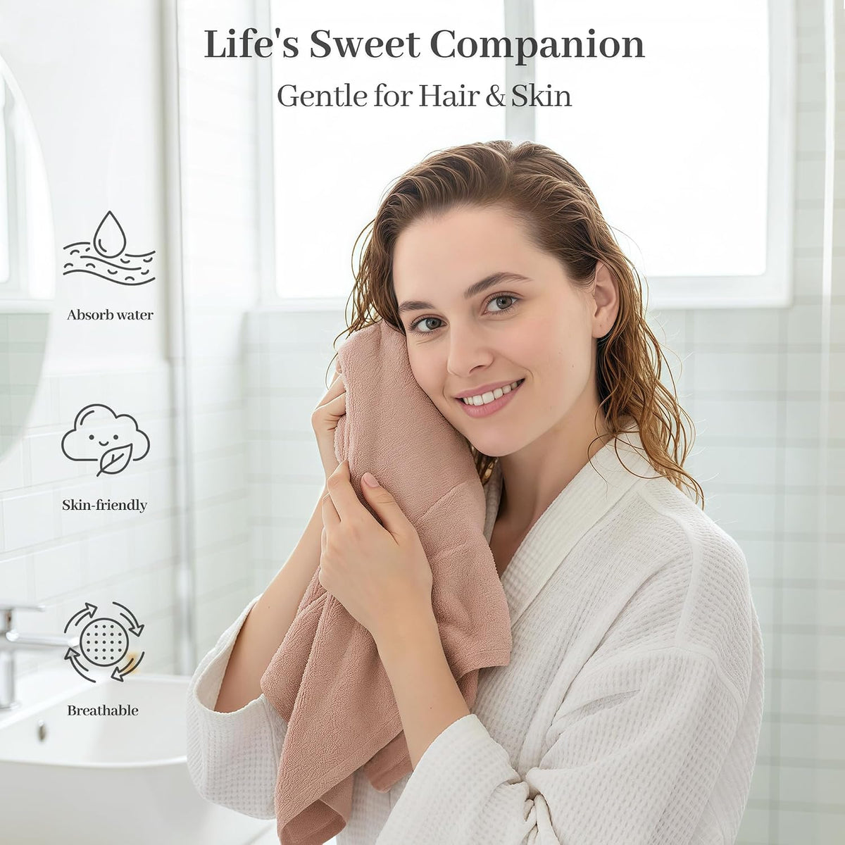 Woman in a white robe pressing a dusty pink textured towel against her cheek in a bathroom setting. Text reads 'Life's Sweet Companion - Gentle for Hair & Skin' with icons for Absorb water, Skin-friendly, and Breathable.