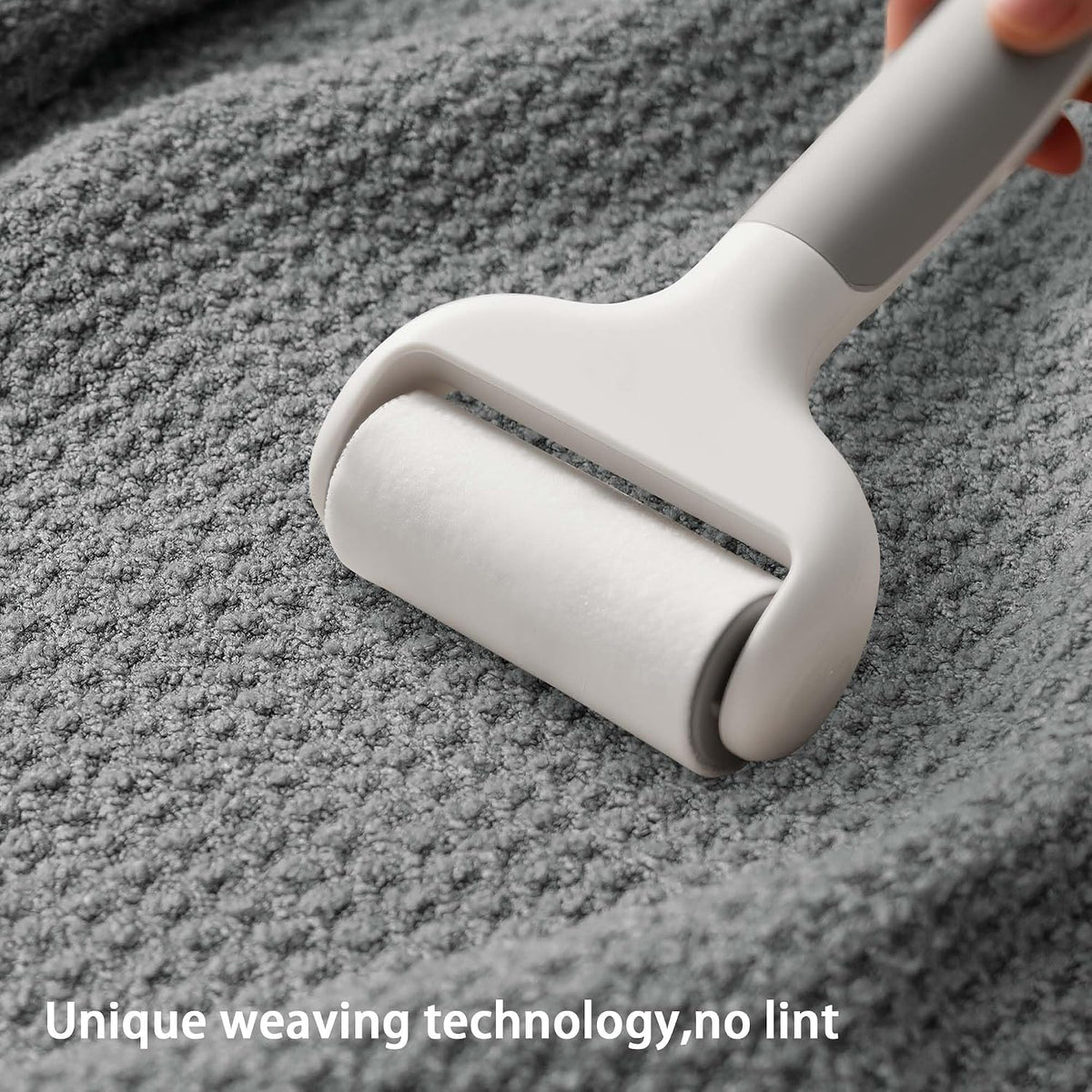 A light gray lint roller being pressed onto a textured gray fabric surface, held by a hand. White text overlay reads 'Unique weaving technology, no lint'.
