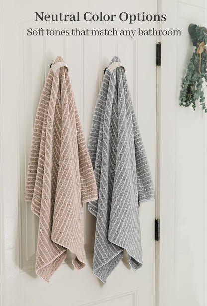 Two textured bath towels hanging on hooks on a white door -- one blush pink and one gray -- both featuring a diagonal stripe pattern. Text reads 'Neutral Color Options: Soft tones that match any bathroom.'