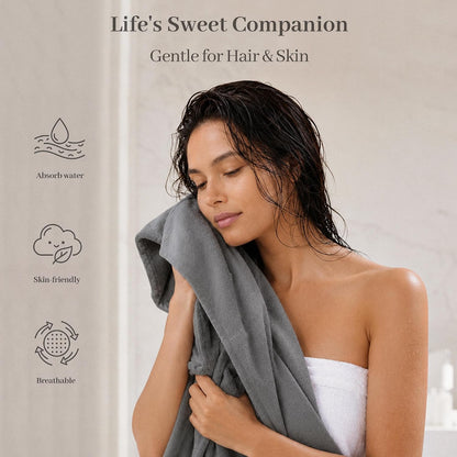 Promotional banner for a gray cotton hair towel. A woman with wet dark hair presses the soft gray towel to her cheek, eyes closed. Left side shows three icons with labels: Absorb water, Skin-friendly, and Breathable. Text reads 'Life's Sweet Companion' and 'Gentle for Hair & Skin.'