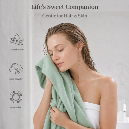 Promotional lifestyle image of a light green cotton towel held against the face by a woman with wet hair, wrapped in a white towel. Left side shows three icons with labels: Absorb water, Skin-friendly, and Breathable. Text reads 'Life's Sweet Companion, Gentle for Hair & Skin'.
