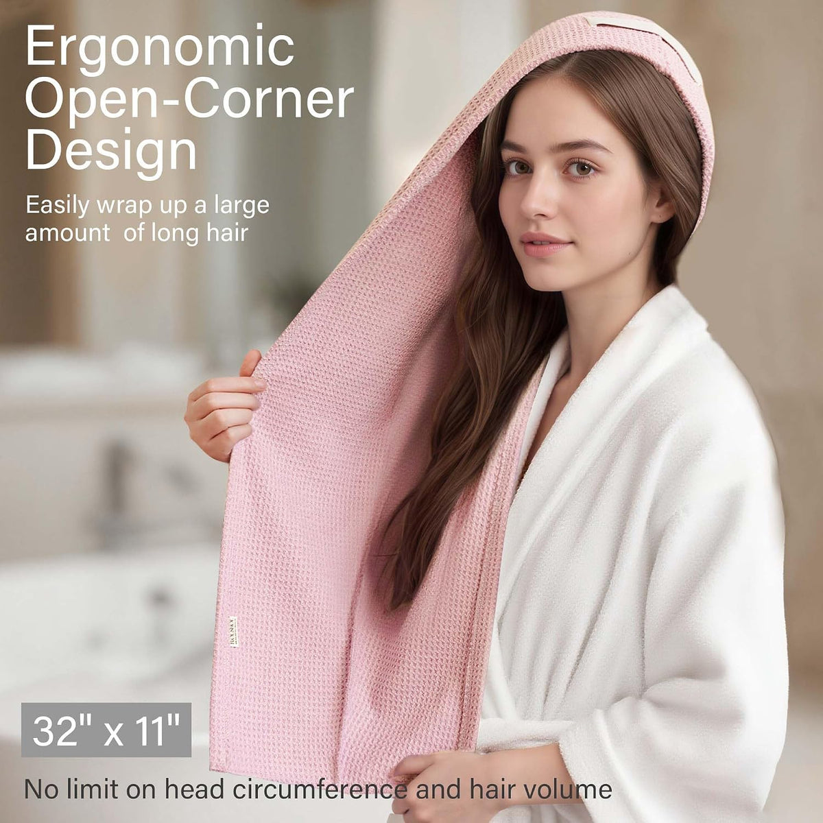 Pink waffle-weave hair towel wrap shown in use on a woman with long hair wearing a white robe. Text reads 'Ergonomic Open-Corner Design' and dimensions '32" x 11"'. Blurred bathroom background.