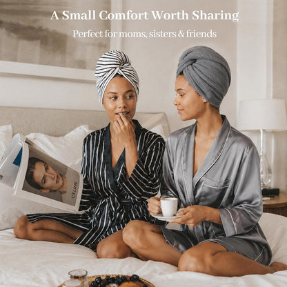 Two women sitting on a bed wearing hair towel wraps -- one in black-and-white stripes, one in solid gray -- paired with robes. Text reads 'A Small Comfort Worth Sharing. Perfect for moms, sisters & friends.'