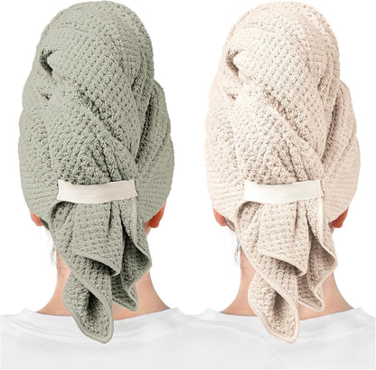Two hair towel wraps shown from the back, worn on a person's head. Left wrap is sage green, right is light beige/clay. Both feature a waffle-knit texture, a white elastic band closure, and draped fabric at the nape.