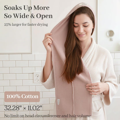 Woman in a waffle-knit robe draping a large blush pink hair towel wrap over her long brown hair. Text reads 'Soaks Up More, So Wide & Open,' '25% larger for faster drying,' '100% Cotton,' and '32.28 x 11.02 inches.'