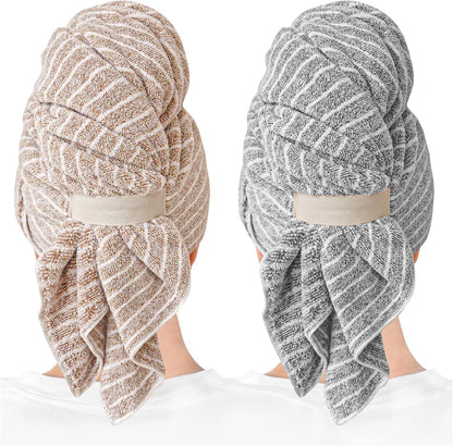 Two hair towel wraps shown worn on the back of a head: one in brown with white stripes (left) and one in gray with white stripes (right). Both feature a twisted turban style secured with an elastic strap and a hanging tail.