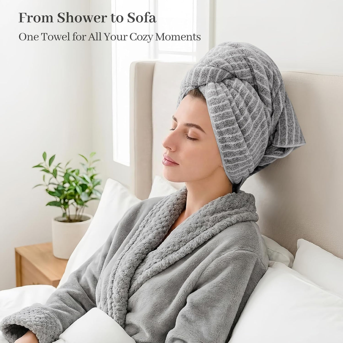 Woman in a gray robe relaxing against a bed headboard with a gray striped microfiber hair towel wrapped in a turban style on her head. Text reads 'From Shower to Sofa - One Towel for All Your Cozy Moments.'