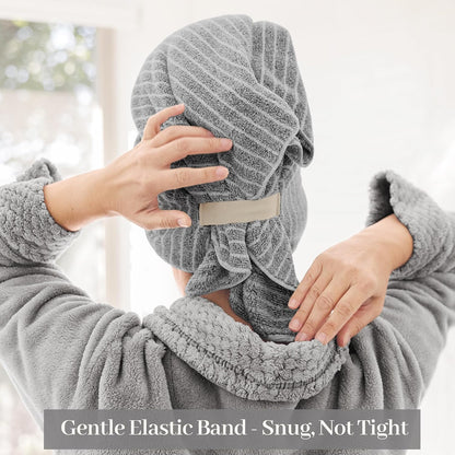 Person seen from behind wearing a grey textured hair towel wrap on their head, adjusting it with both hands. A beige elastic strap is visible at the back. Text overlay reads: Gentle Elastic Band - Snug, Not Tight.