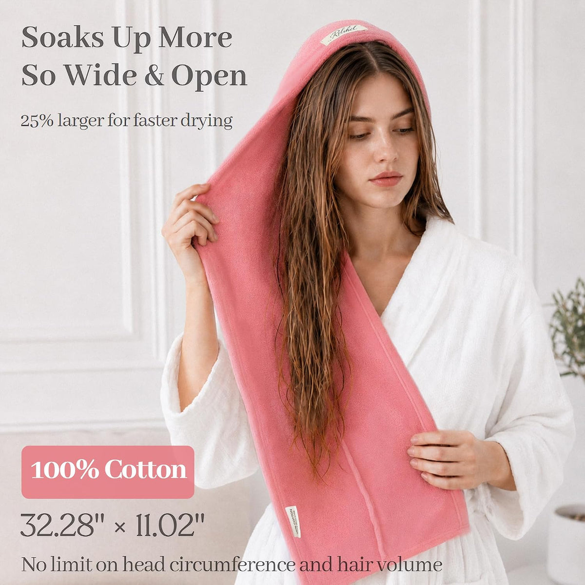 Pink cotton hair drying towel wrap shown draped over a woman's wet hair. Text states 'Soaks Up More, So Wide & Open,' '25% larger for faster drying,' '100% Cotton,' '32.28 x 11.02 inches,' and 'No limit on head circumference and hair volume.'