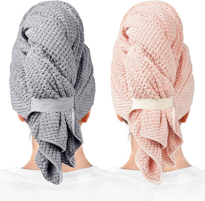 Two hair towel wraps worn on heads, shown from behind. Left wrap is gray with a textured waffle pattern and elastic band closure; right is light pink with the same design. Both have loose fabric draping at the nape.